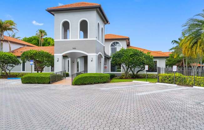 A white building with a red roof and a grey tiled courtyard in front.