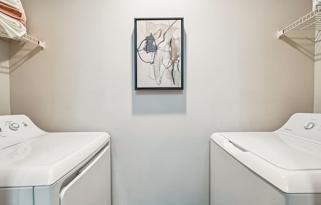 A laundry room with two washing machines and a picture hanging on the wall.