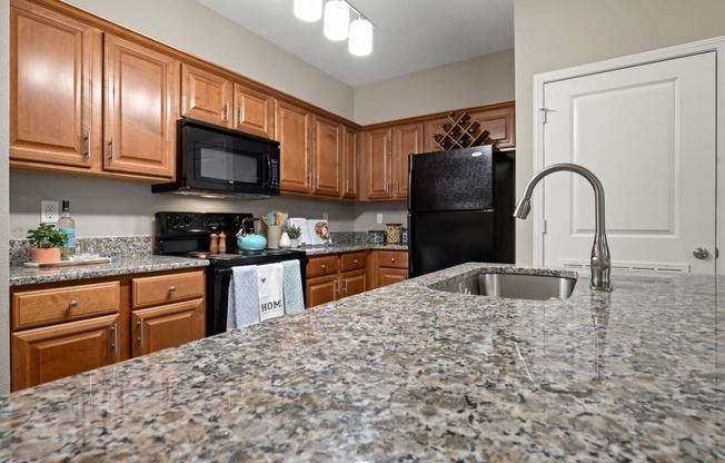 Riverstone - Kitchen withGranite Countertops,Black Appliances, andWooden Cabinets