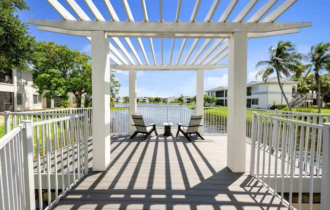 a patio with a pergola and chairs overlooking a body of water