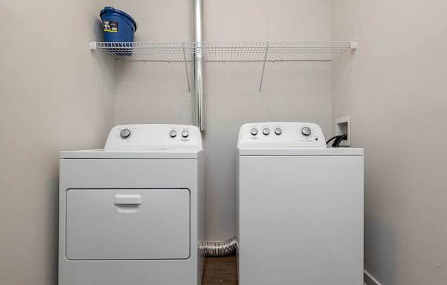 A laundry room with two washing machines and a shelf above them.