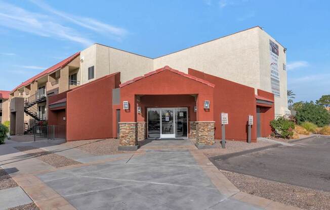 A building with a red and beige exterior and a stone pillar in front at Urban WalkApartments on 6th Avenue, Arizona