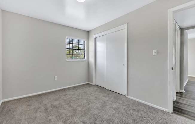 a bedroom with white walls and carpet and a door to a closet