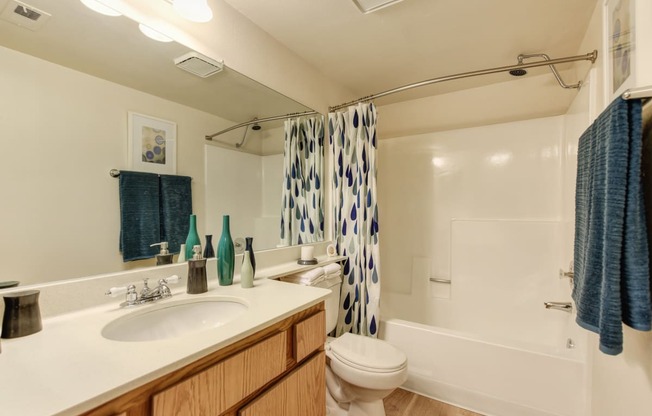 Bathroom with sink vanity and tub/shower combination.  There are accent colors of blue and teal with the bath towels and shower curtains. 