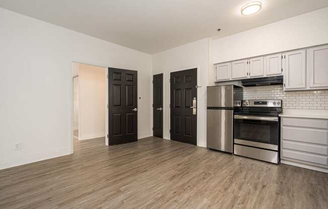 an empty living room with a kitchen with stainless steel appliances