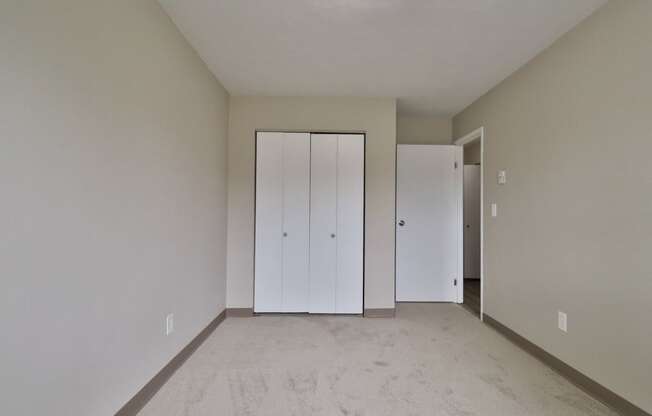 a living room with white walls and a carpet and two closets