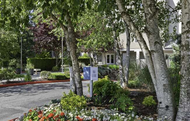 Entrance with trees and flowers in front of property building at West Mall Place Apartment Homes, Everett, WA