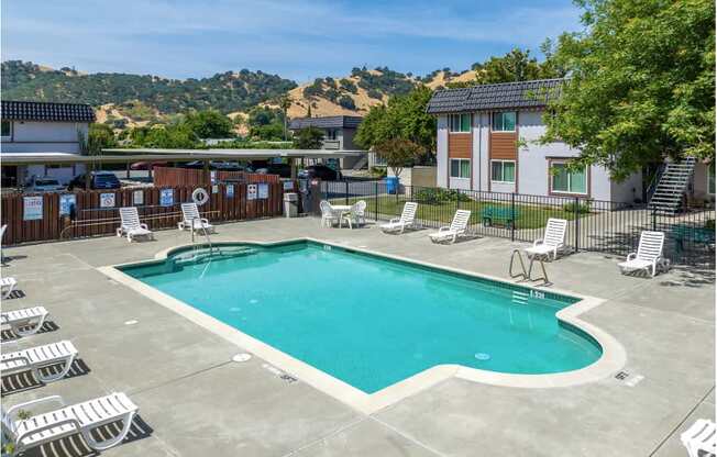 A large swimming pool surrounded by lounge chairs and a hillside in the background.