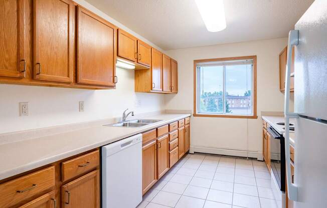 A kitchen with wooden cabinets and a white dishwasher. Fargo, ND Summit Point Apartments