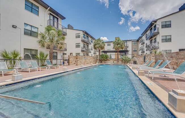 Resort style pool with stone wall and lounge chairs at Vue Live Oak Apartments, Dallas, TX