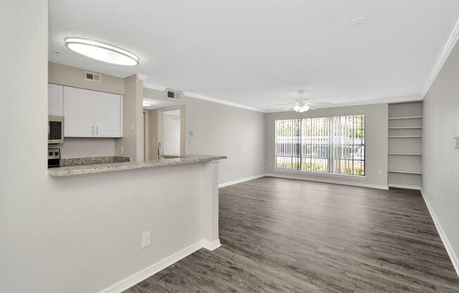 Spacious living area with hardwood-style flooring, large windows allowing natural light, and a ceiling fan. The kitchen features granite countertops, modern cabinetry, and overlooks the dining space, creating an open-concept layout suitable for entertaining or relaxing.