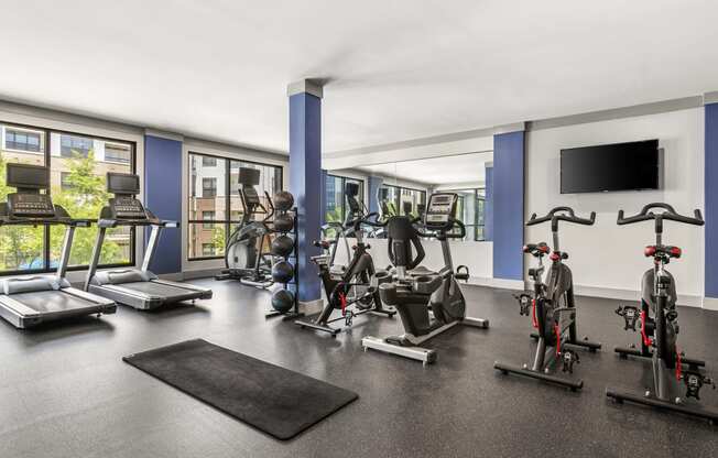 a gym with treadmills and other exercise equipment in a room with windows