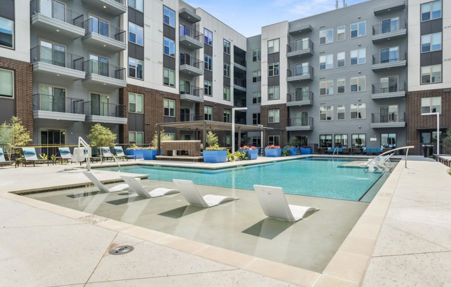 an apartment swimming pool with chairs in front of an apartment building