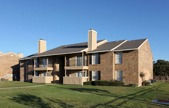 a brick apartment building with balconies and a lawn at Wymberly Pointe, Grand Prairie, TX, 75052