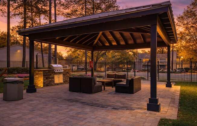 A pavilion with a stone floor and a roof is surrounded by trees.