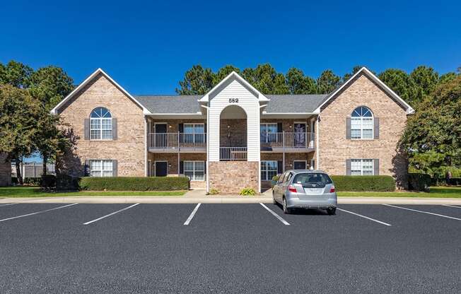A silver car is parked in front of a two-story brick building.