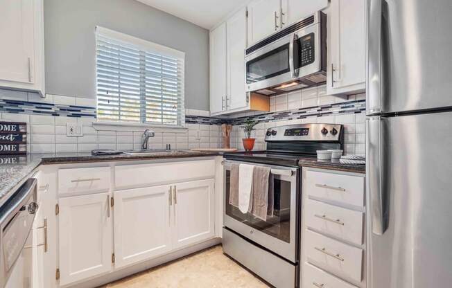 San Jose CA Apartments for Rent - Los Gatos Creek - Kitchen with Stainless-Steel Appliances, White and Blue Backsplash, a Window, and White Cabinetry