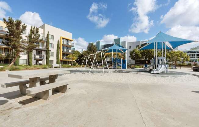 A playground with a blue canopy and a slide is surrounded by buildings.