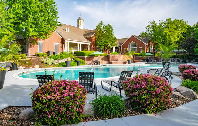 A pool surrounded by a garden with a house in the background.