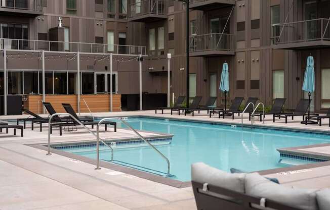 A pool surrounded by chairs and umbrellas in front of a building.