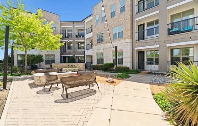 A sunny day at a modern apartment complex with a brick patio and seating area.