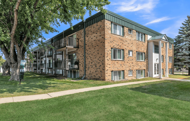 a brick apartment building with green grass and trees