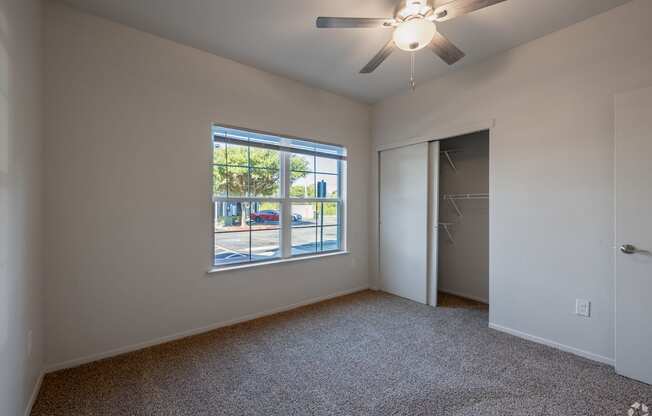A room with a ceiling fan and a window overlooking a street.