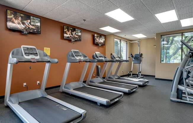 Fitness room with treadmills facing TVs on an orange wall