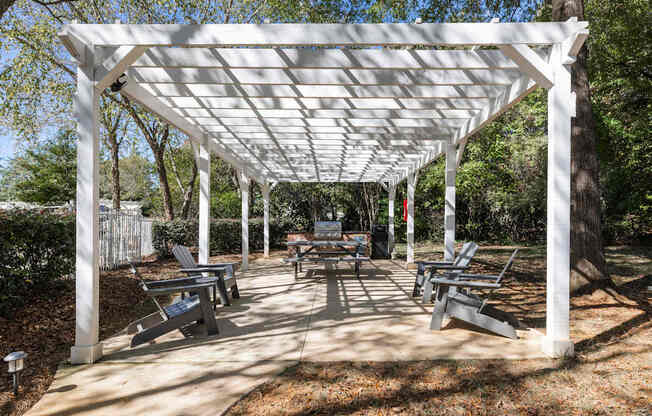 A white pergola with benches is set up in a park.