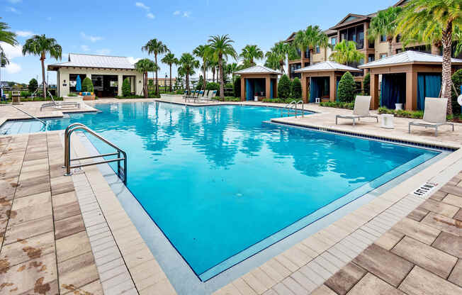 a resort style swimming pool with lounge chairs and palm trees in the background