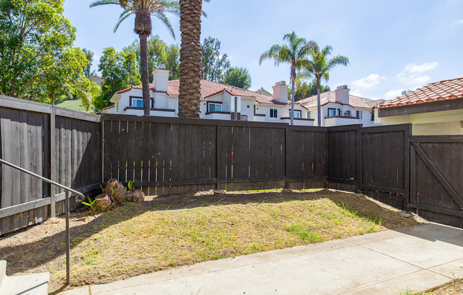 a fenced in yard with palm trees and a house in the background