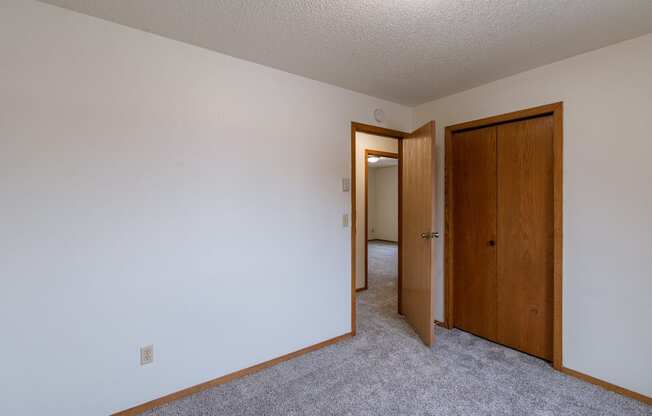 a bedroom with a closet and a door to a hallway. Fargo, ND Crescent Park Apartments