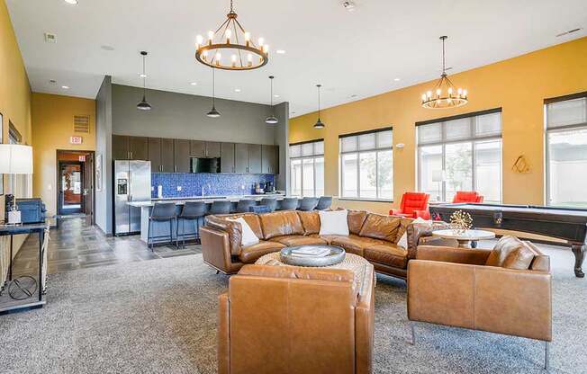 A clubhouse kitchen with large island and several bar stools, and a lounge area with a leather couch, chairs, and a pool table.