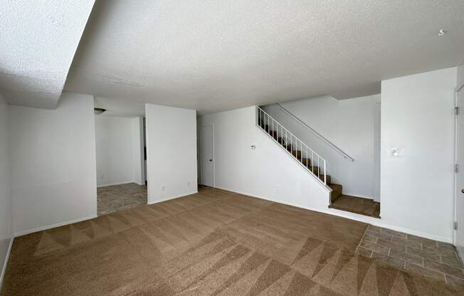 a living room with a carpeted floor and a staircase in the background