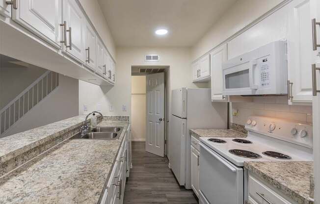Kitchen with white cabinets and white appliances and large pass-through window in a 2 bedroom, 1.5 bath 1084 sq ft, 2-floor townhome at The Biltmore Apartments located in the Vickery Midtown neighborhood of Dallas, TX.