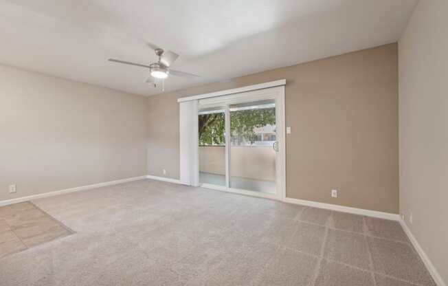 an empty living room with a large window and a ceiling fan