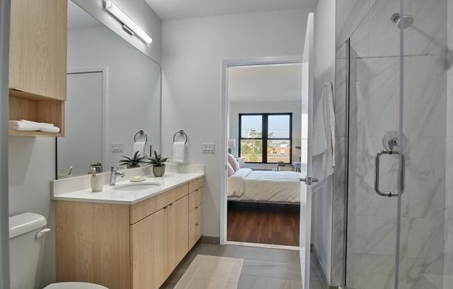 Sleek bathroom at The Mint Rahway with modern fixtures, a large mirror, and a view into a well-lit bedroom, ideal for luxury apartment rentals near Newark Airport.
