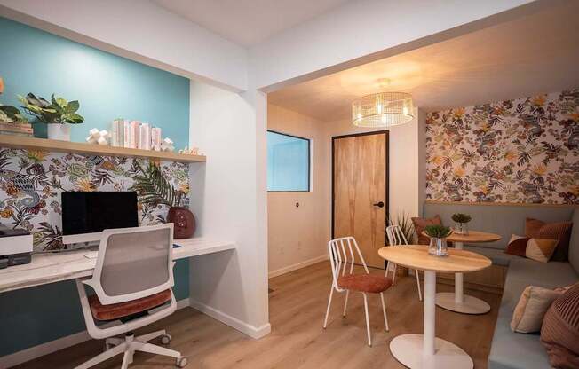 A room with a desk, chairs, and a couch with a floral wallpaper.