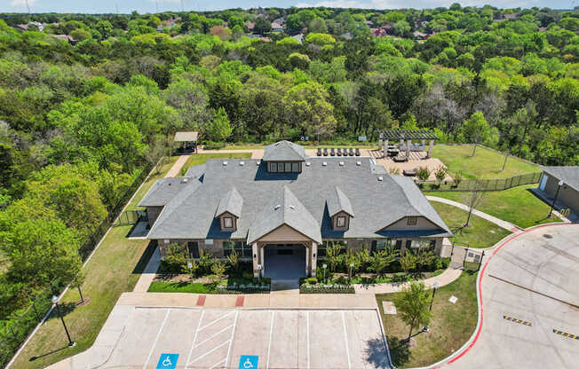 A large building with a grey roof is surrounded by a green lawn and trees.