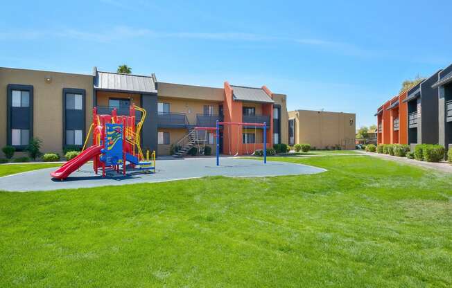 Outdoor, brightly colored playground and swings surrounded by large grassy area for kids to play