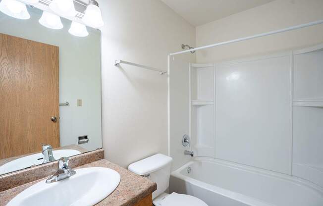 A white bathroom with a toilet, sink, and bathtub. West Fargo, ND Saddlebrook Apartments