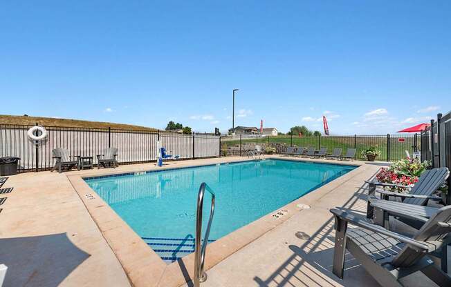 A swimming pool surrounded by a fence and lounge chairs.
