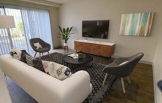 A living room with a white couch, a black and white rug, a wooden cabinet, a TV, and a painting on the wall.