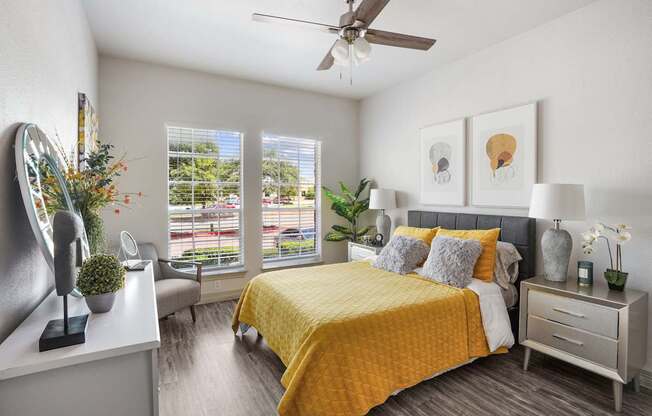 A bedroom with a yellow bedspread and a ceiling fan.