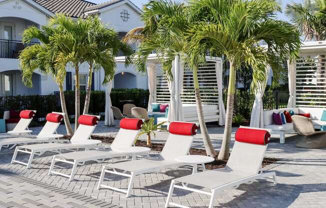 a row of white lounge chairs with red pillows in front of a resort