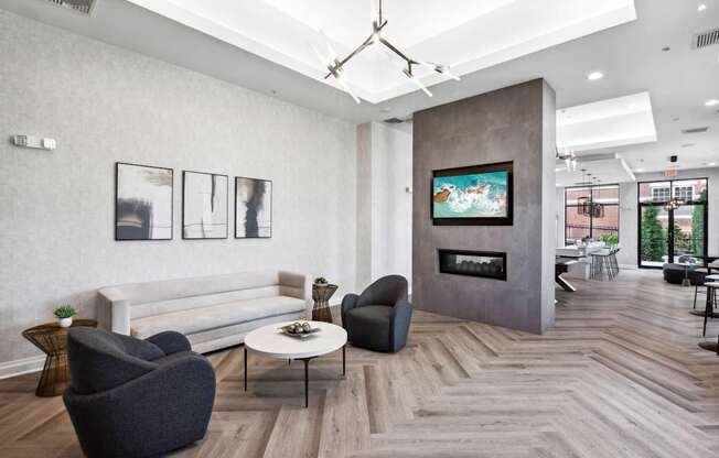 A living room with a grey couch, a black chair, a coffee table, and a fireplace with a painting above it.