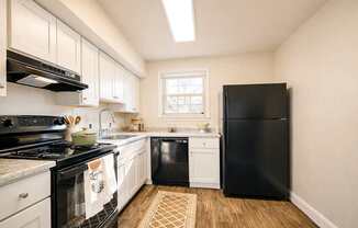 A black refrigerator stands in a kitchen with white cabinets and a black stove.