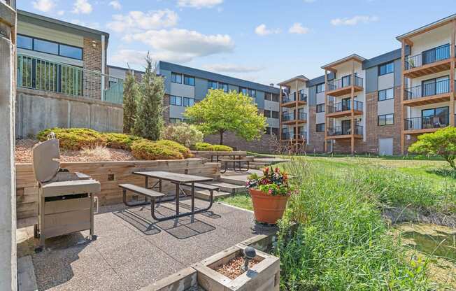 A patio with a table and chairs is surrounded by a garden and apartment buildings.