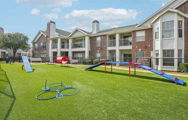 A playground with a slide, swings, and a climbing frame is situated in front of a large apartment building.