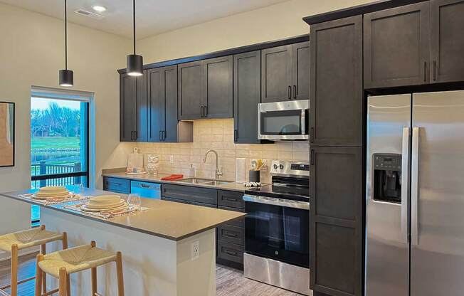 a kitchen with dark cabinets, a tile backsplash, quartz countertops, stainless steel appliances, and a micro-island